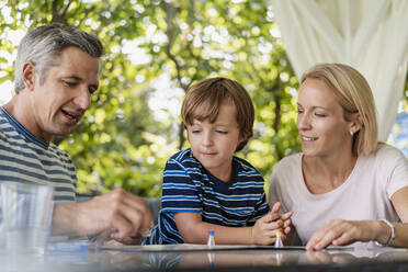 Glückliche Eltern und Sohn spielen ein Brettspiel auf der Terrasse - DIGF08138