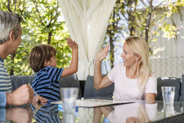 Glückliche Mutter und Sohn, die sich nach einem gewonnenen Spiel auf der Terrasse die Hände reichen - DIGF08139