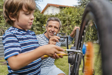 Father and son repairing a bicycle in garden - DIGF08150