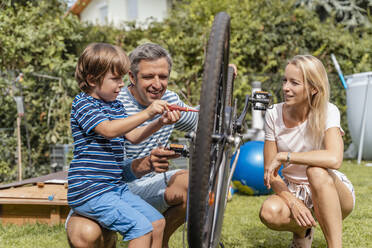 Family repairing a bicycle together in garden - DIGF08152