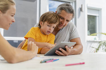 Vater, Mutter und Sohn machen Hausaufgaben und benutzen gemeinsam ein Tablet auf der Terrasse - DIGF08179