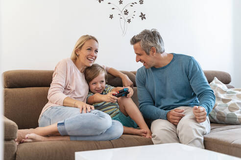 Glückliche Eltern mit ihrem Sohn, der zu Hause auf der Couch ein Videospiel spielt - DIGF08184