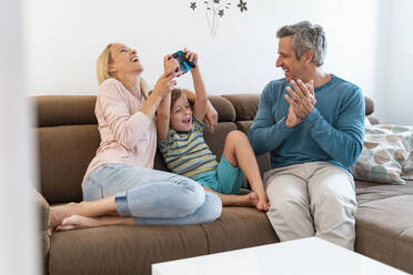 Happy parents with son playing video game on couch at home - DIGF08185