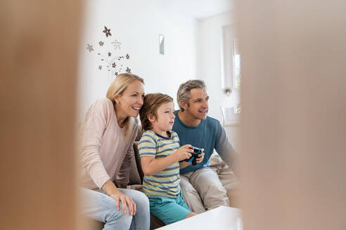 Glückliche Eltern mit ihrem Sohn, der zu Hause auf der Couch ein Videospiel spielt - DIGF08187