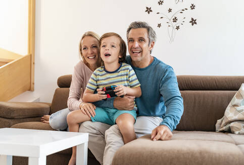 Glückliche Eltern mit ihrem Sohn, der zu Hause auf der Couch ein Videospiel spielt - DIGF08188