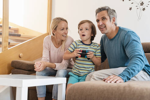 Glückliche Eltern mit ihrem Sohn, der zu Hause auf der Couch ein Videospiel spielt - DIGF08189