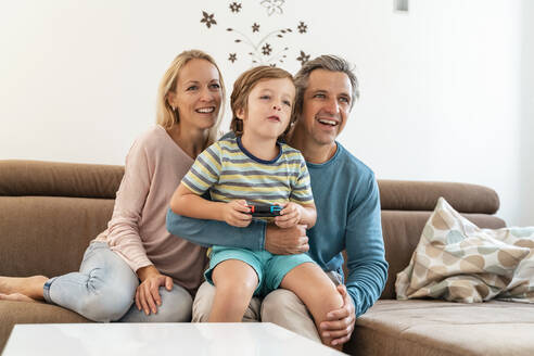 Glückliche Eltern mit ihrem Sohn, der zu Hause auf der Couch ein Videospiel spielt - DIGF08191