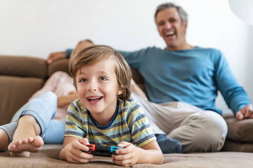 Junge liegt auf der Couch zu Hause und spielt ein Videospiel, während die Eltern zusehen - DIGF08196