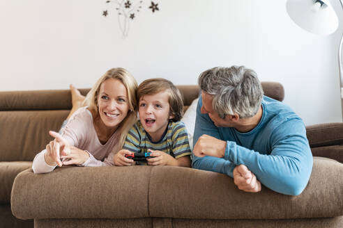 Glückliche Eltern mit ihrem Sohn, der zu Hause auf der Couch ein Videospiel spielt - DIGF08197