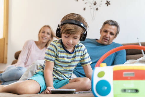 Familie auf der Couch zu Hause mit einem Jungen, der mit Kopfhörern Musik hört - DIGF08200