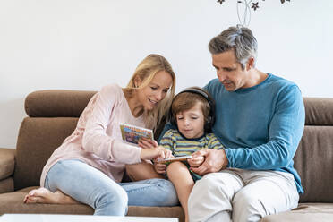 Family on couch at home with boy listening to music with headphones - DIGF08203