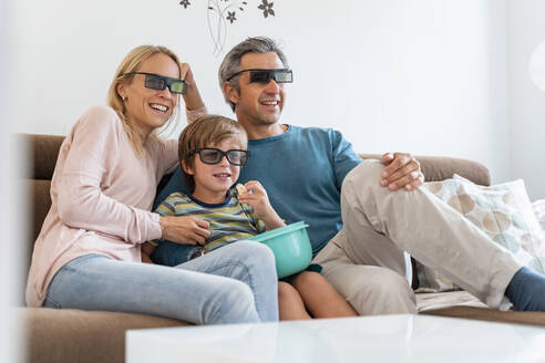 Vater, Mutter und Sohn mit 3d-Brille auf der Couch zu Hause beim Fernsehen - DIGF08209