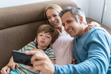 Father, mother and son taking a selfie on couch at home - DIGF08211