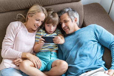 Father, mother and son using cell phone on couch at home - DIGF08212