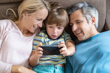 Father, mother and son using cell phone on couch at home - DIGF08213