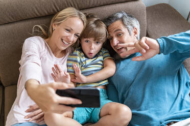 Father, mother and son taking a selfie on couch at home - DIGF08214