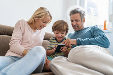 Father, mother and son using cell phone on couch at home - DIGF08217