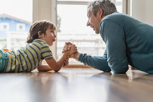 Father and son lying on the floor at home arm wrestling - DIGF08220