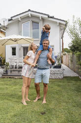 Portrait of father with wife carrying son on shoulders in garden - DIGF08227