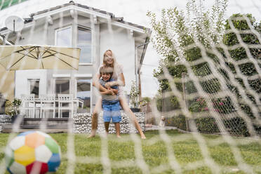Glückliche Mutter und Sohn spielen Fußball im Garten - DIGF08249