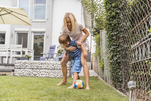 Happy mother and son playing football in garden - DIGF08252