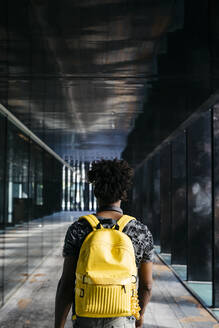 Back view of man with yellow backpack walking through a passage, Barcelona, Spain - JRFF03691