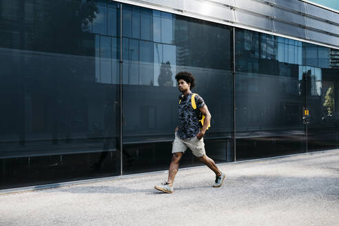 Man with yellow backpack and headphones walking down the street, Barcelona, Spain - JRFF03696