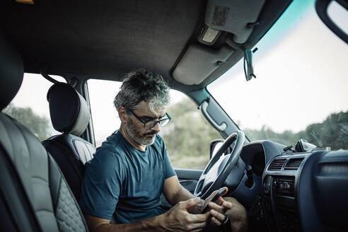 Älterer Mann sitzt in seinem Geländewagen und überprüft sein Smartphone - OCMF00650