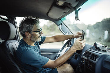 Mature man sitting sitting in his off-road vehicle checking his smartphone - OCMF00651