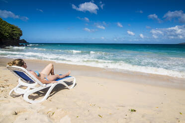 Frau entspannt auf Liegestuhl am Strand gegen blauen Himmel, Grande Anse, Grenada, Karibik - RUNF02992