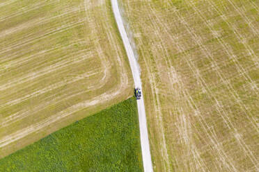 Luftaufnahme eines Traktors auf einem unbefestigten Weg inmitten eines landwirtschaftlichen Feldes, Münsing, Deutschland - LHF00684