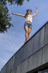 Lächelnde junge Frau balanciert auf einem Brückengeländer - STSF02232