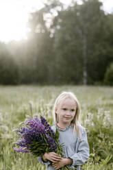 Portrait of blond little girl with bunch of lupines on a meadow - EYAF00475