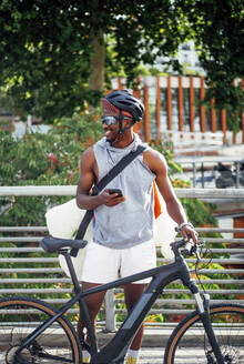 Glücklicher Fahrradkurier mit Handy, der sich umschaut - OCMF00674