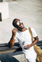 Glücklicher junger Mann mit Kopfhörern und Mobiltelefon in der Stadt - OCMF00690