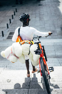 Rückansicht eines Fahrradkuriers, der einen Teddybären ausliefert - OCMF00691