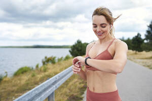 Porträt einer fitten Frau, die beim Joggen im Freien ihre Smartwatch überprüft - BSZF01390