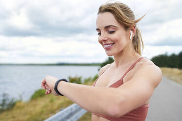 Porträt einer fitten Frau, die beim Joggen im Freien ihre Smartwatch überprüft - BSZF01391