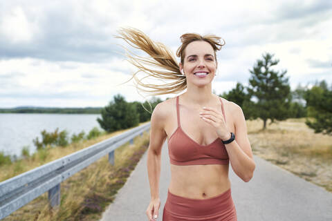 Porträt einer lächelnden, sportlichen Frau beim Joggen im Freien, lizenzfreies Stockfoto