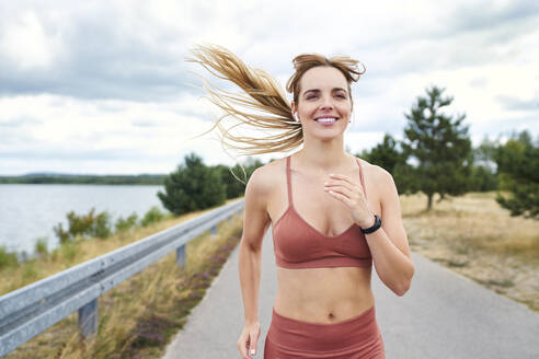 Porträt einer lächelnden, sportlichen Frau beim Joggen im Freien - BSZF01395