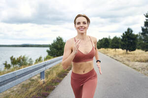 Porträt einer lächelnden, sportlichen Frau beim Joggen im Freien - BSZF01396