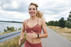 Porträt einer lächelnden, sportlichen Frau beim Joggen im Freien - BSZF01397