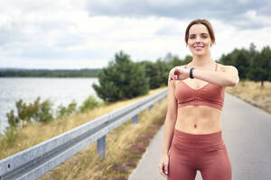 Porträt einer fitten Frau, die beim Joggen im Freien ihre Smartwatch überprüft - BSZF01398