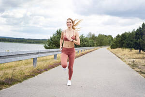 Lächelnde sportliche Frau beim Joggen am See - BSZF01400