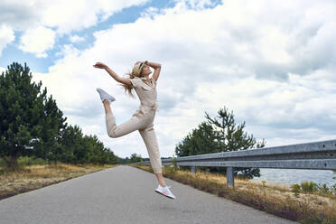 Cheerful woman jumping on rural road - BSZF01423