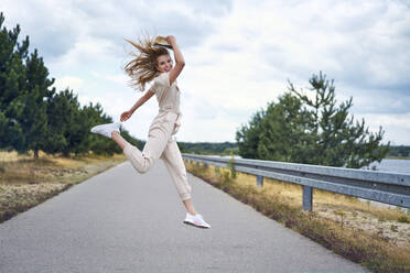 Cheerful woman jumping on rural road - BSZF01424