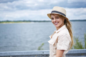 Porträt einer lächelnden Frau mit Hut am Seeufer - BSZF01430