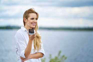 Glückliche Frau mit Handy am Seeufer - BSZF01445