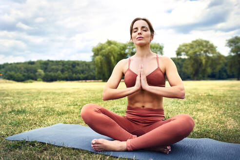 Frau übt Yoga im Park und meditiert - BSZF01464