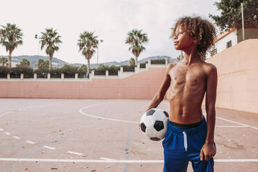 Boy holding a soccer ball standing on a soccer field - LJF00980